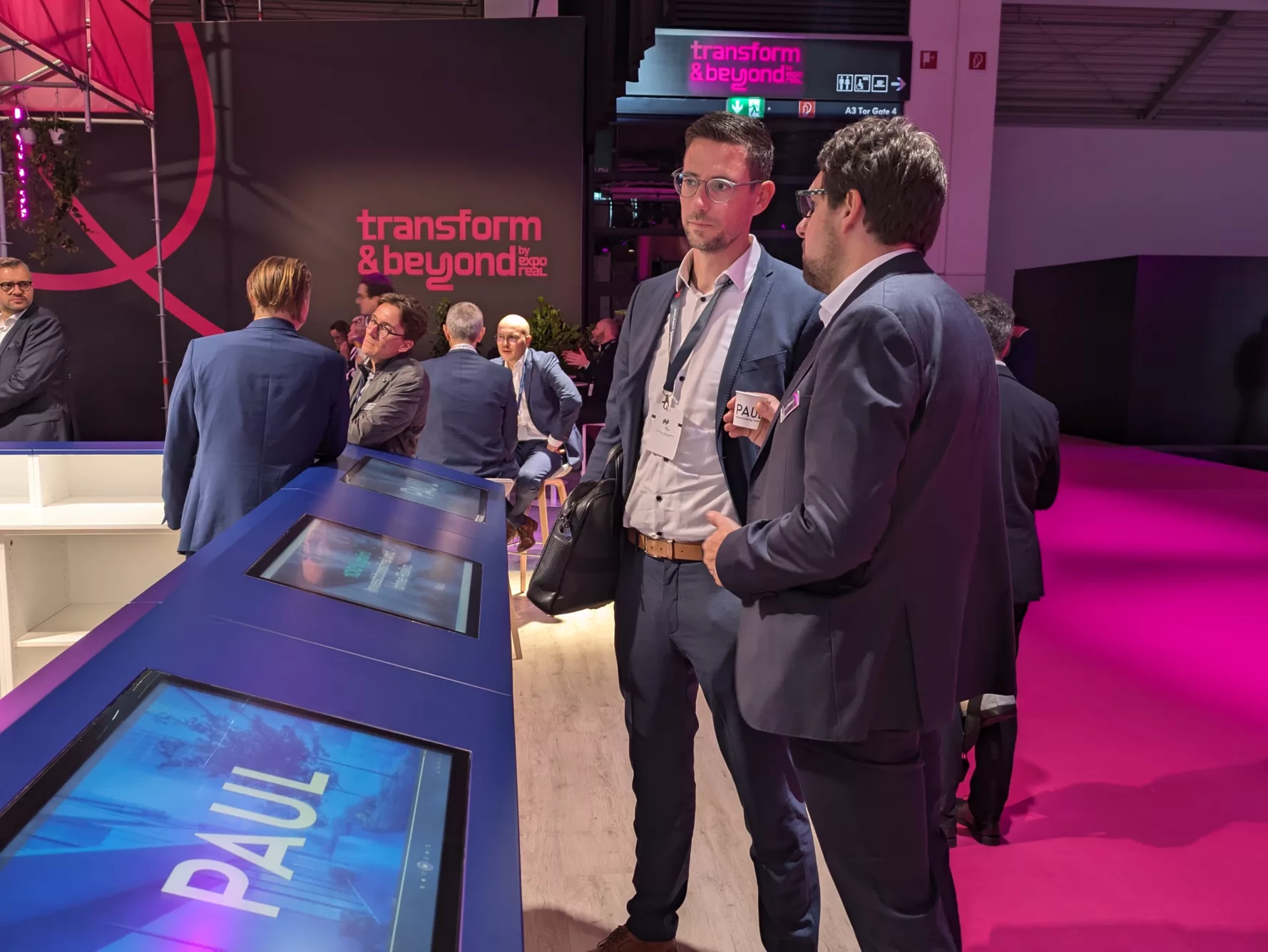 Personen vor dem Touch Screen Monitoren auf dem PAUL Messestand